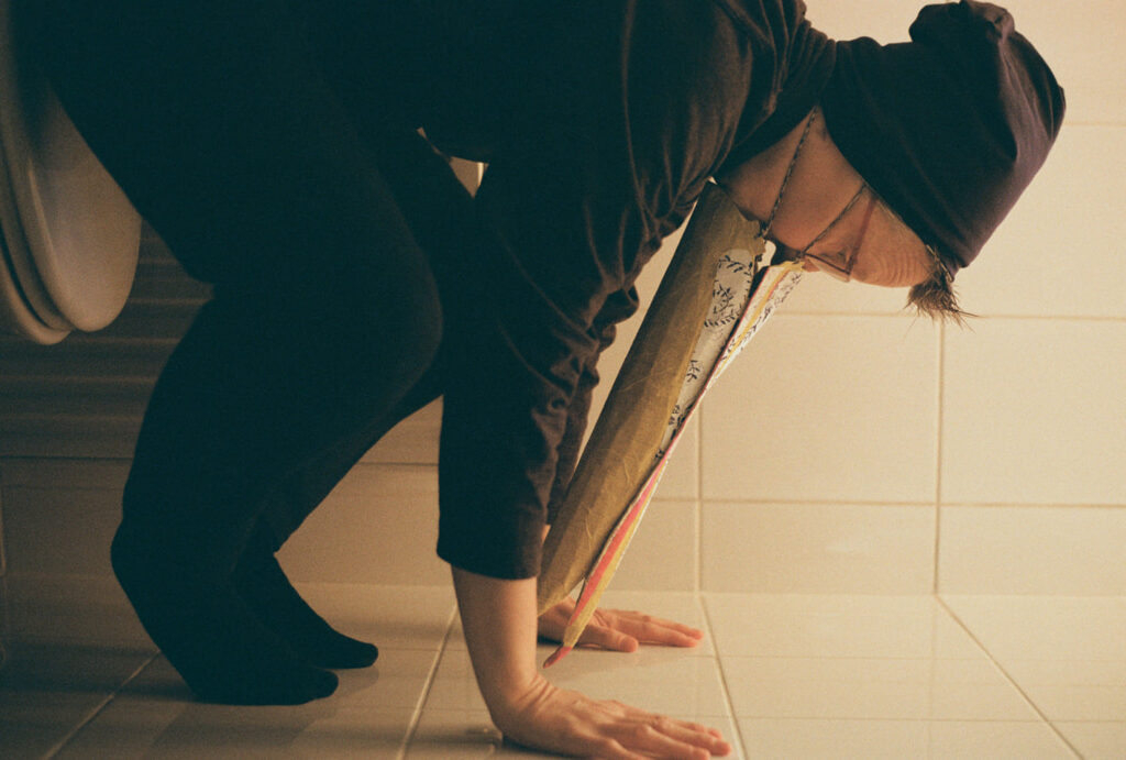 Photography of a person with a pelican's beak pushing hands against tiles
