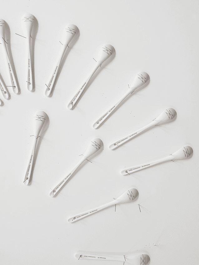 Spoons made of porcelain fixed on a grayish-white background, the back of each spoon shows a blade of a razor barb wire, detail