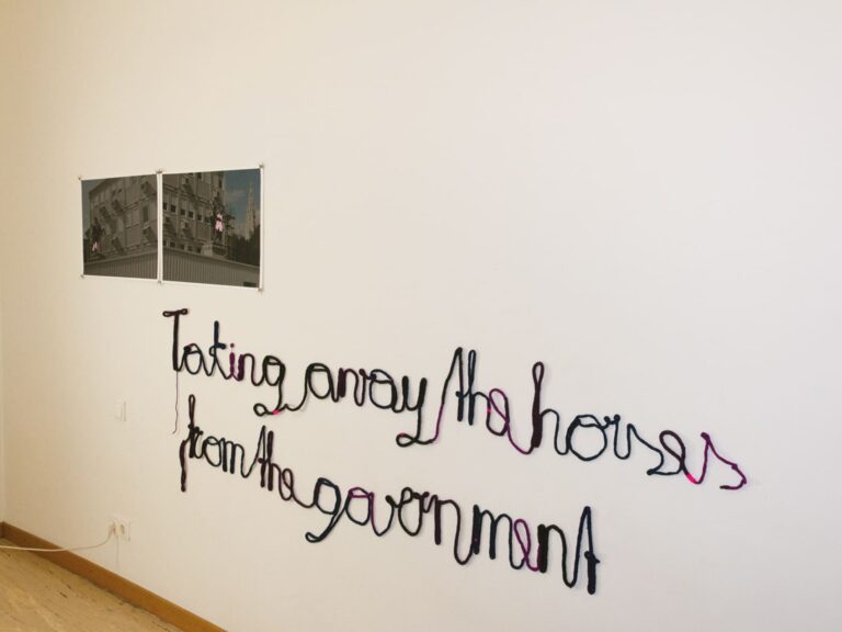 beide Fotografien nebeneinander an einer Wand montiert; unterhalb befindet sich der Schriftzug "Taking away the horses from the government" aus gestrickten Wollschnueren geschrieben