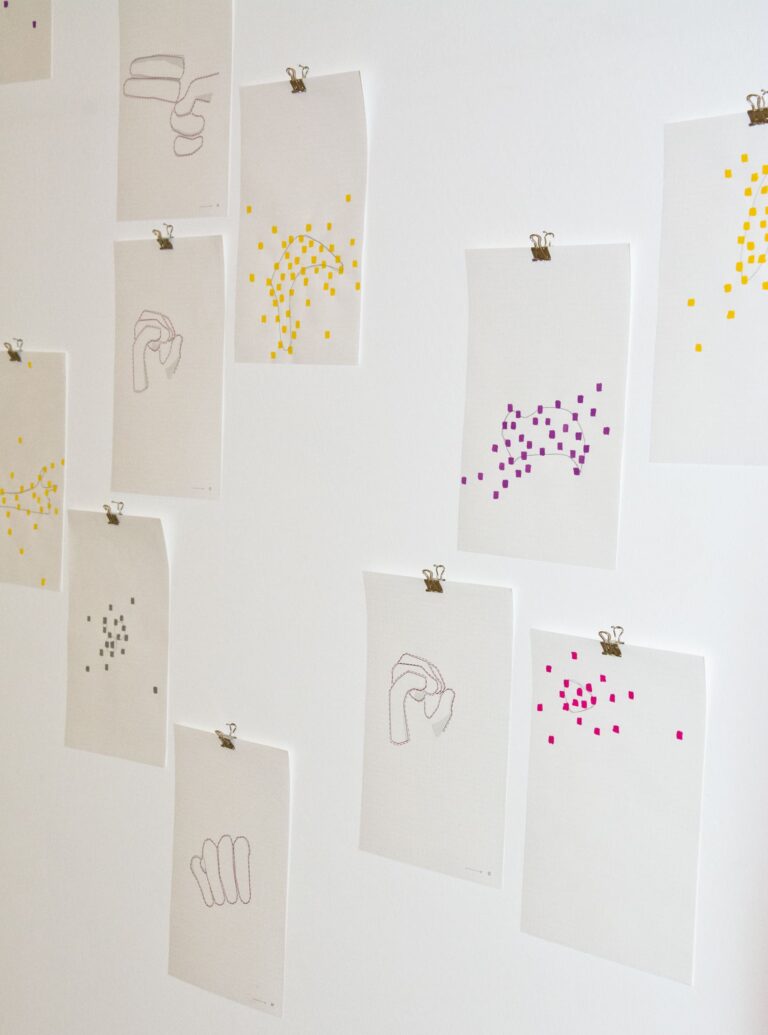 Detail of "Twisting codes", different sheets of paper with dots and abstract forms fixed on a wall; four sheets with letters of the Austrian finger alphabet "h", "o", "m" and "o"